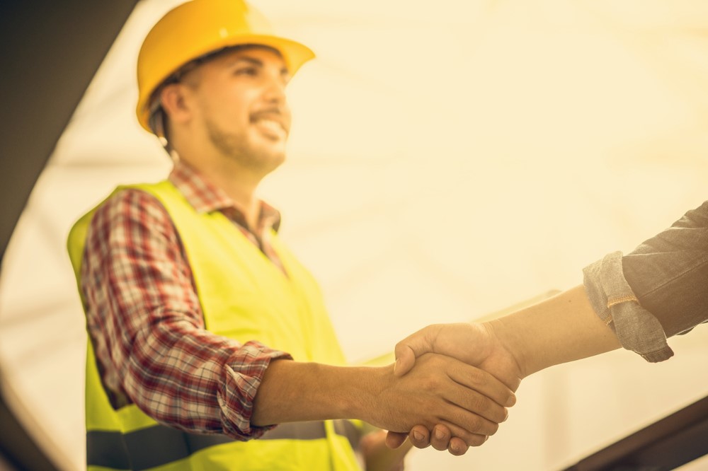 Construction worker wearing yellow hard hat and vest, shaking hands with another person