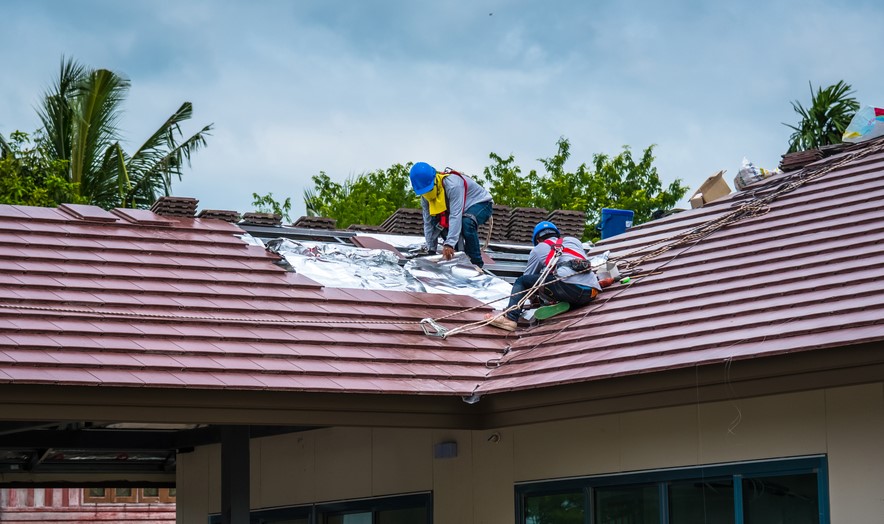 Two roofers in harnesses fixing a portion of a tile roof